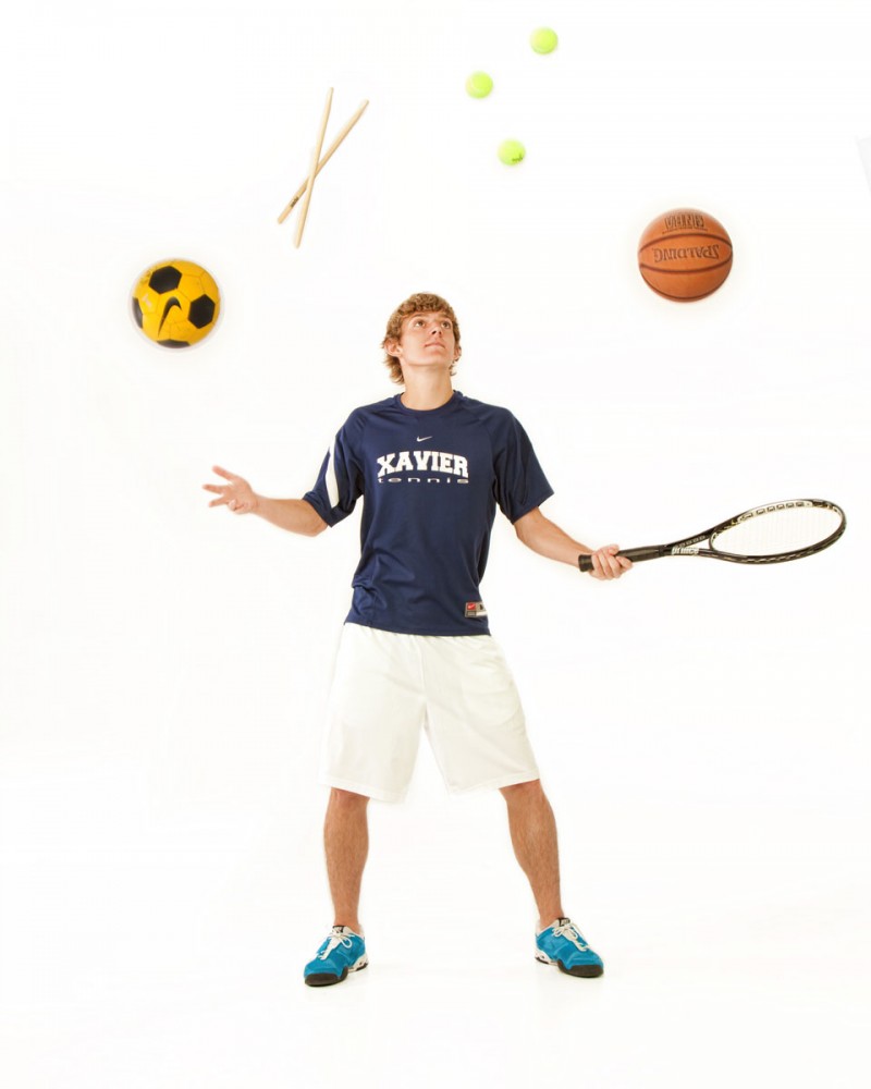 A young man appears to be juggling a soccer ball, a basketball, drum sticks and a tennis racket