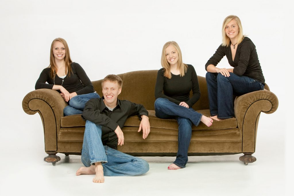 Family of 4 brothers and sisters, siblings in a casual, contemporary modern arrangement on a couch as a gift for mom.