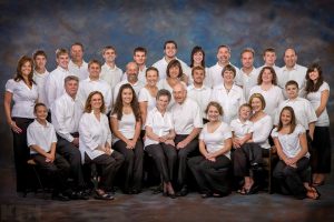 A family of 3 generations and over 30 people poses comfortably wearing white shirts.