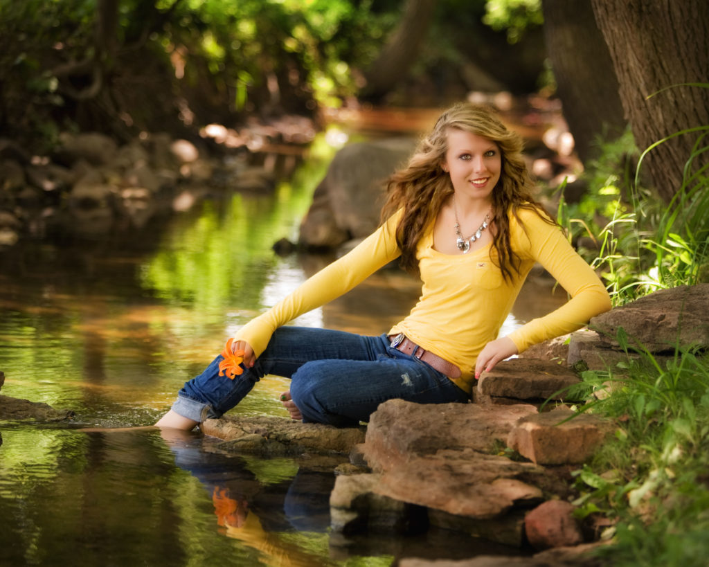 High school senior girl posing sitting on a rock, with her feet in a stream at KenMar's private photo park.  